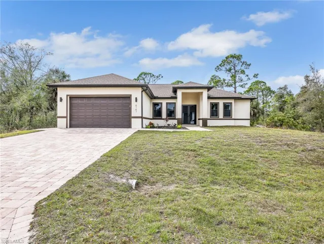 Prairie-style house with stucco siding, a garage, decorative driveway, and a front lawn