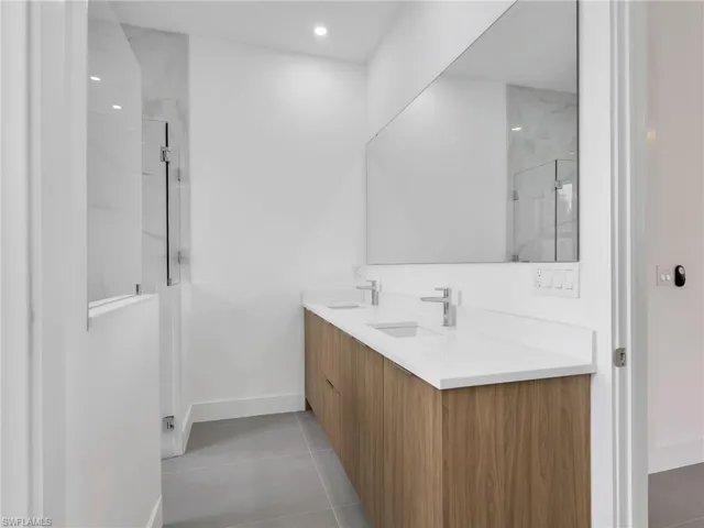 Bathroom with double vanity, light tile patterned floors, recessed lighting, and a marble finish shower