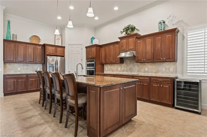 Kitchen featuring hanging light fixtures, crown molding, wine cooler, an island with sink, and appliances with stainless steel finishes