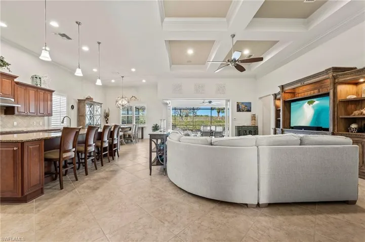 Tiled living room with ceiling fan, crown molding, a high ceiling, and coffered ceiling
