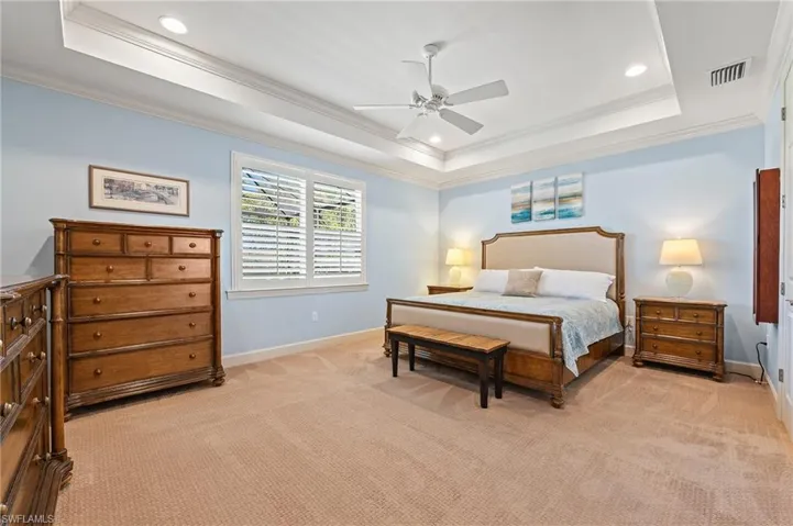 Bedroom with ceiling fan, a raised ceiling, crown molding, and light carpet