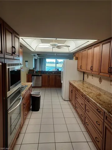 Kitchen featuring light stone counters, ceiling fan, refrigerator, and wood finish cabinets