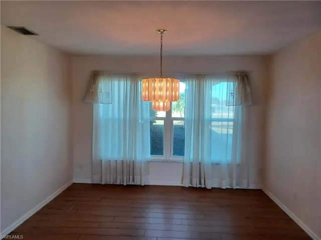 Unfurnished dining area with dark wood-style floors and hanging lights