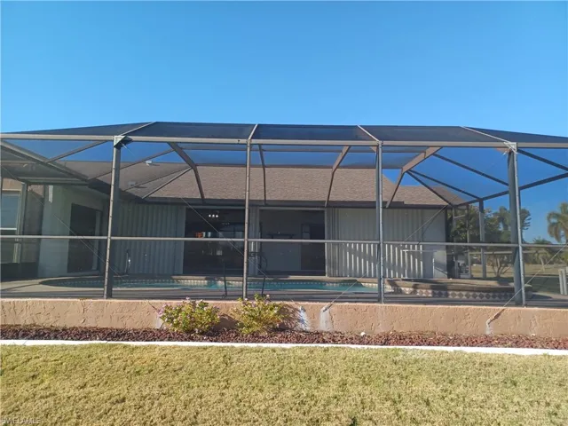 Back of property with a sunroom, a lanai, an outdoor pool, and a lawn