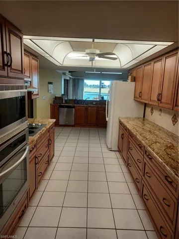 Kitchen with wood finish cabinets, light stone countertops, fridge, a ceiling fan, and wall oven