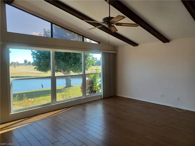 Spare room featuring lofted ceiling with beams, a ceiling fan, a water view, and wood finished floors