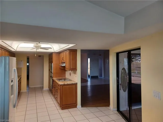 Kitchen featuring wood finish cabinets, white fridge with ice dispenser, light tile patterned floors, light stone countertops, and electric cooktop