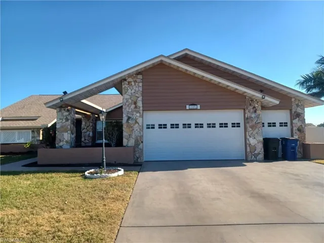 Ranch-style home with stone siding, a front lawn, and driveway