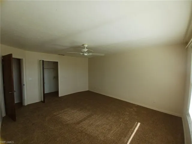 Unfurnished bedroom with dark colored carpet, a spacious closet, and a ceiling fan