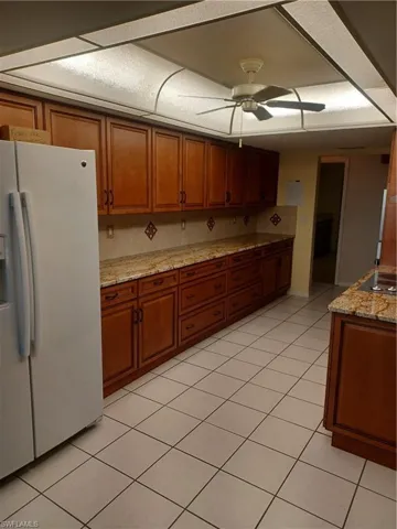Kitchen featuring refrigerator, wood finish cabinetry, light stone counters, and a ceiling fan