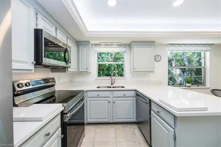 Kitchen featuring gray cabinetry, a sink, appliances with stainless steel finishes, a peninsula, and light countertops