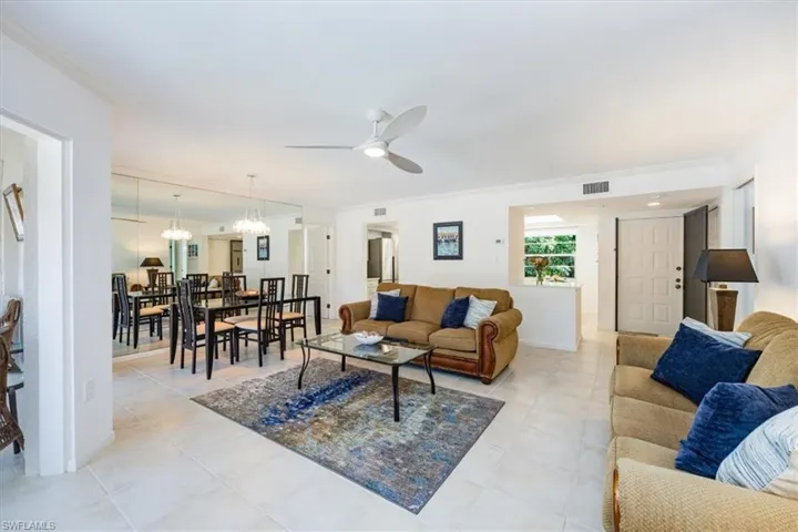 Living room featuring light tile patterned floors, visible vents, ceiling fan with notable chandelier, and ornamental molding