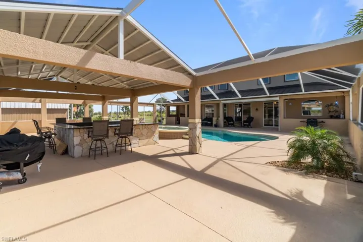 Expansive outdoor living area featuring a covered patio, a built-in outdoor bar with seating, and a swimming pool