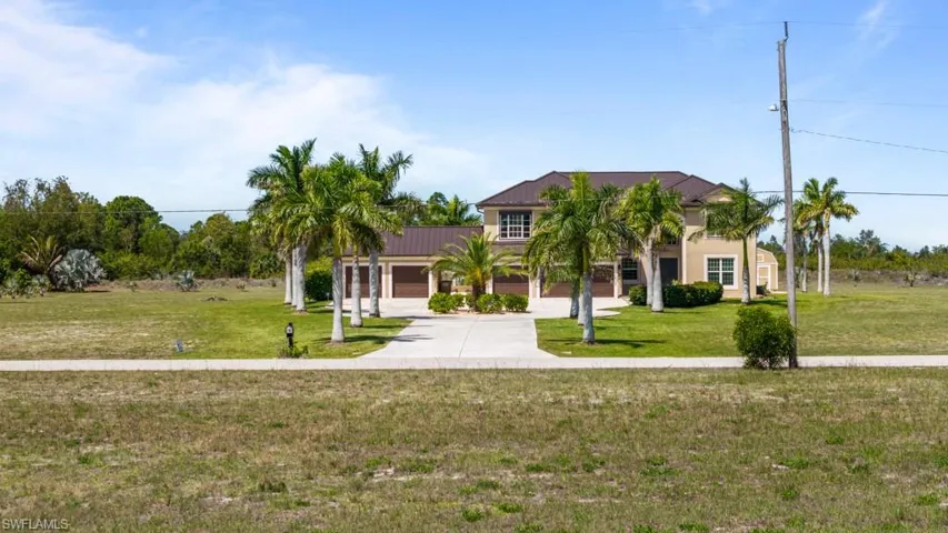 The property features a two-story exterior with a brown roof and light-colored siding, a paved driveway, and palm trees