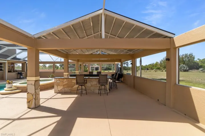 Expansive outdoor living area featuring a covered patio, a built-in stone bar with seating, and views of the surrounding green space