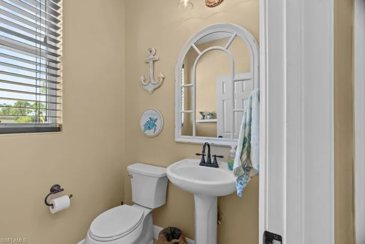 The bathroom features a pedestal sink with a dark faucet, a toilet, and a window with blinds