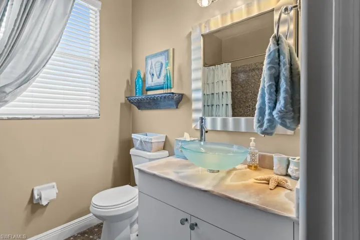 Bathroom featuring a clear glass vessel sink, a vanity with a light-colored countertop, and a window with white blinds