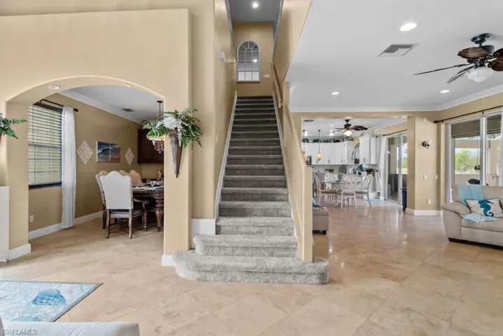 This property features tiled flooring throughout the main level, a carpeted staircase leading to the upper level, and an arched entryway to an additional room