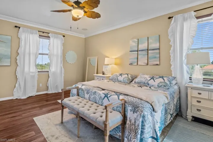 This bedroom features hardwood floors, a ceiling fan, and two windows with blinds and curtains