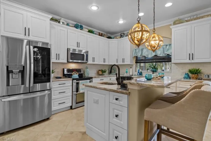 The kitchen features white cabinetry, stainless steel appliances, and a kitchen island with a breakfast bar