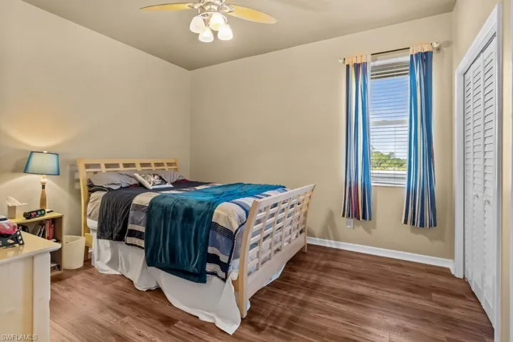 This space features wood-style flooring, a window with blinds and drapes, and a ceiling fan with integrated lighting