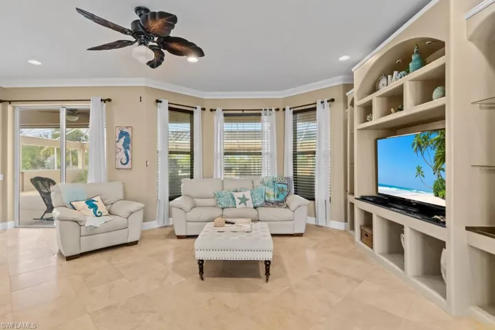 Living area with light-colored tile flooring, a ceiling fan, and bay windows featuring blinds