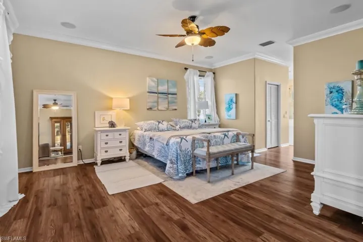 Bedroom featuring hardwood style flooring, a ceiling fan with light fixture, and crown molding
