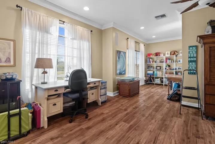 This versatile space features wood-style flooring, crown molding, recessed lighting, and large windows with blinds