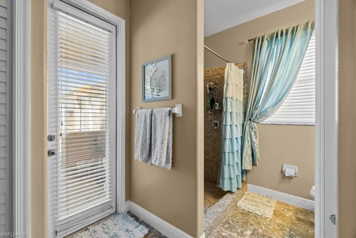 Bathroom featuring a full-glass door with blinds, textured shower walls, and a shower with a tiered curtain