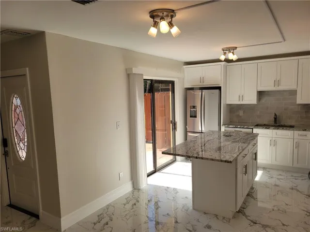 Kitchen with light stone countertops, stainless steel fridge, backsplash, sink, and a center island