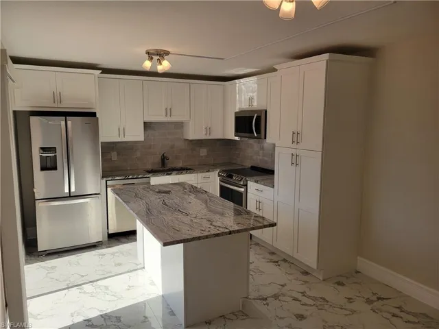 Kitchen with a center island, sink, appliances with stainless steel finishes, light stone counters, and white cabinetry