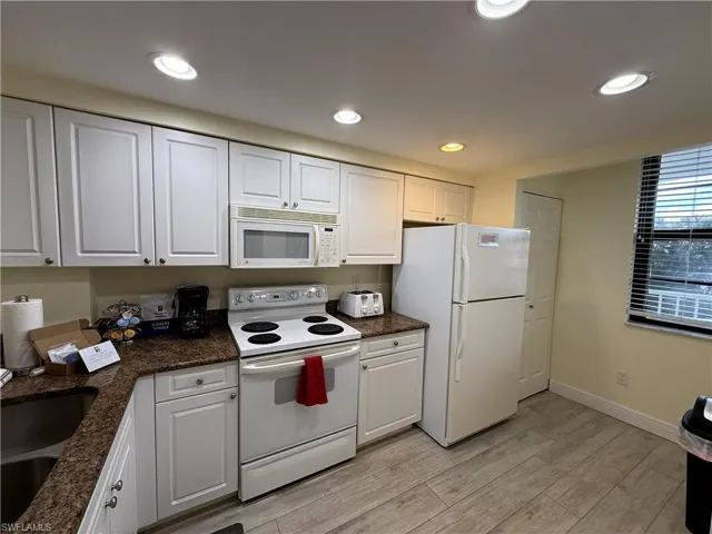 Kitchen featuring white appliances, white cabinets, light wood-style flooring, recessed lighting, and dark stone counters