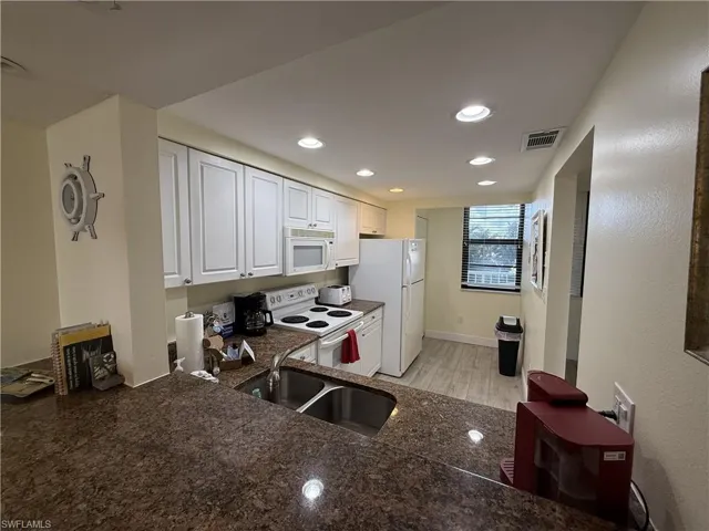 Kitchen featuring white appliances, white cabinets, light wood-style flooring, recessed lighting, and dark stone counters