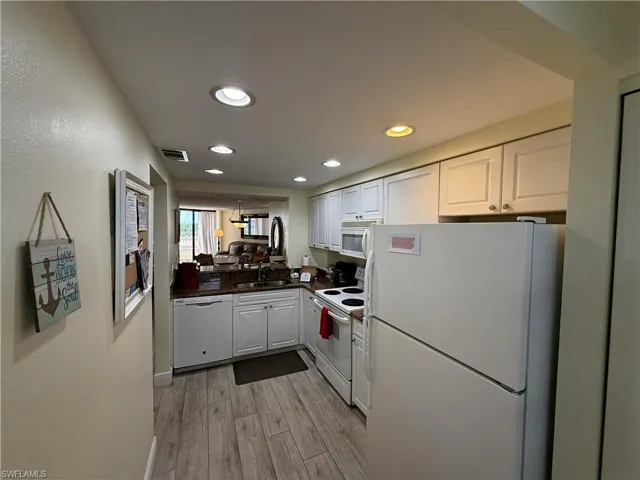 Kitchen with white appliances, white cabinets, light wood finished floors, recessed lighting, and dark stone counters