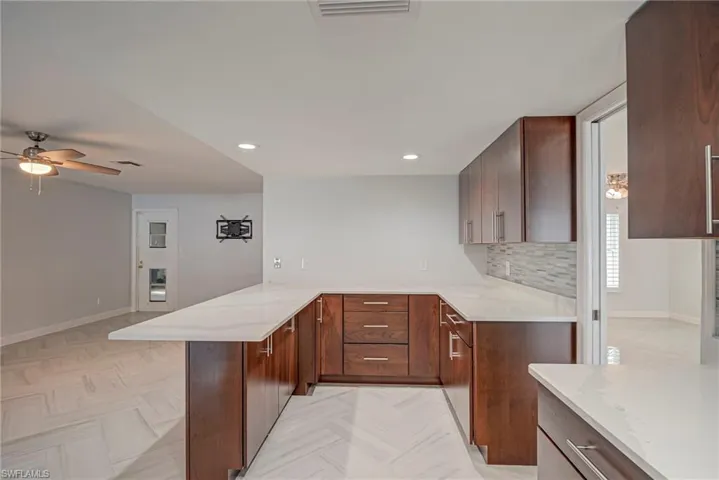 Kitchen with backsplash, light stone countertops, a peninsula, ceiling fan, and recessed lighting