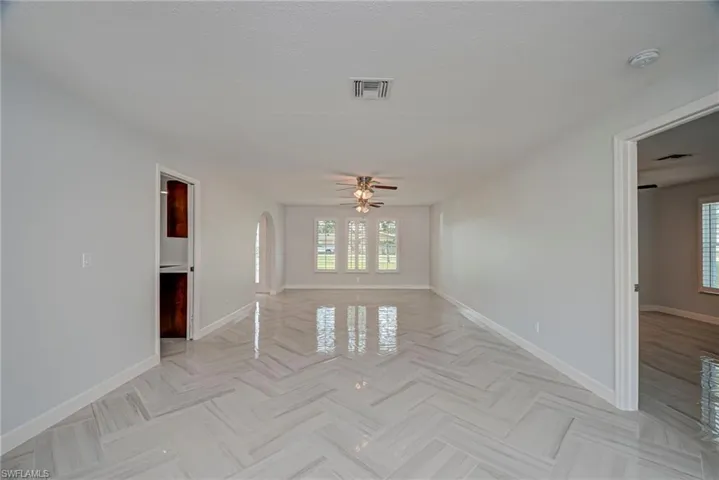Empty room featuring arched walkways, a ceiling fan, and a textured ceiling