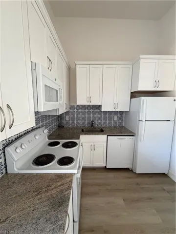 Kitchen featuring white appliances, white cabinetry, tasteful backsplash, and light wood-style floors