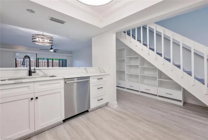 Kitchen featuring crown molding, white cabinetry, sink, stainless steel dishwasher, and light hardwood / wood-style floors