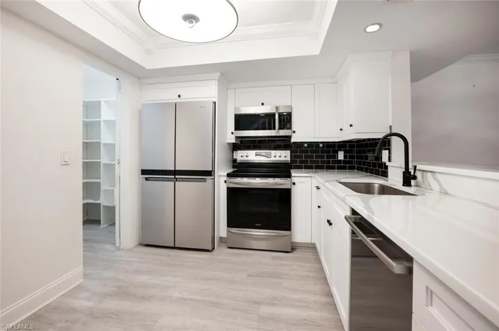 Kitchen featuring appliances with stainless steel finishes, white cabinetry, sink, and decorative backsplash