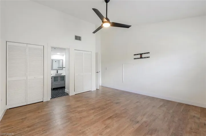 Unfurnished bedroom featuring light wood-type flooring, high vaulted ceiling, ceiling fan, multiple closets, and ensuite bathroom