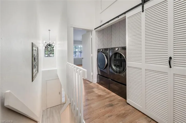 Clothes washing area with washer and dryer, a barn door, a chandelier, and light hardwood / wood-style floors