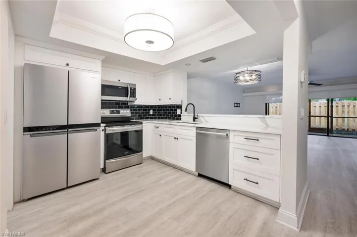 Kitchen with a raised ceiling, white cabinetry, stainless steel appliances, and sink