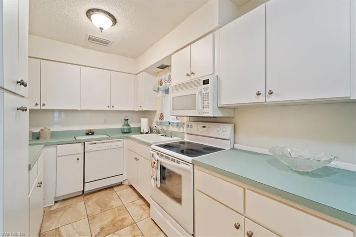 Kitchen featuring white appliances, white cabinets, sink, a textured ceiling, and light tile patterned flooring