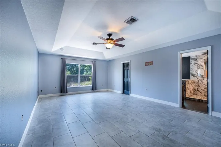 Spare room featuring tile flooring, ceiling fan, and a raised ceiling