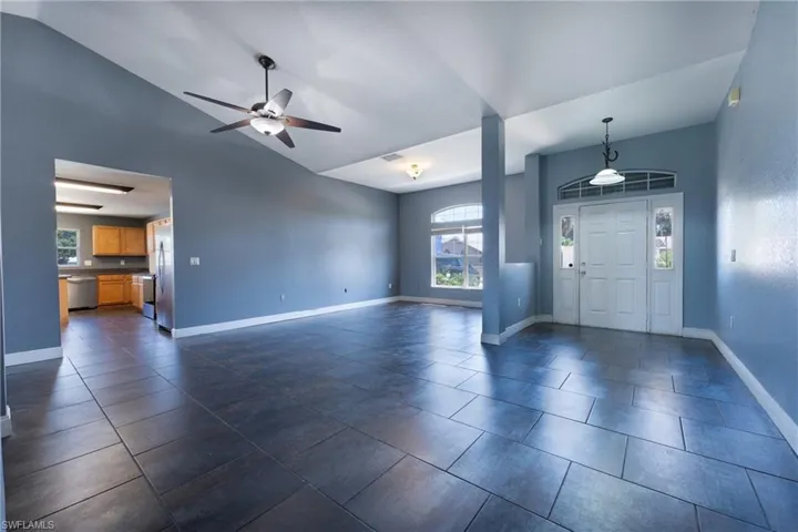Foyer entrance featuring ceiling fan, vaulted ceiling, and dark tile floors