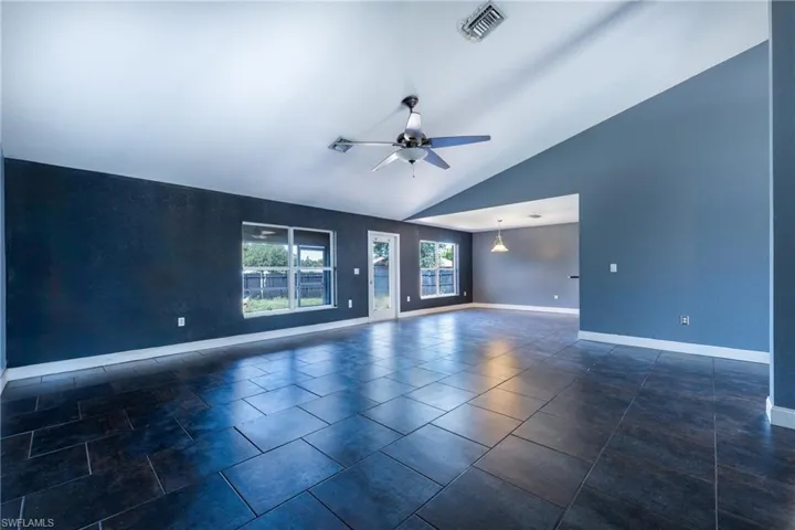 Empty room with high vaulted ceiling, dark tile floors, and ceiling fan