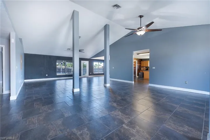 Unfurnished living room featuring high vaulted ceiling, dark tile flooring, and ceiling fan