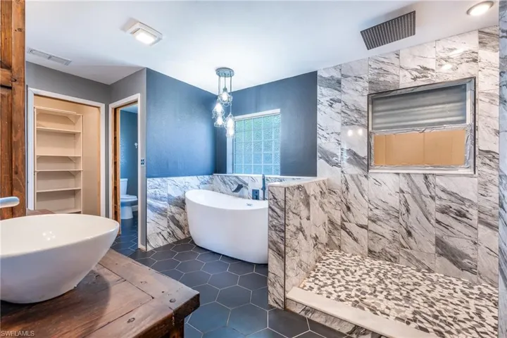 Full bathroom with tile walls, toilet, tile floors, independent shower and bath, and sink