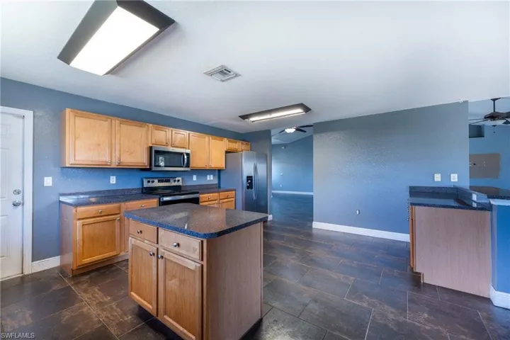Kitchen with dark tile flooring, ceiling fan, and appliances with stainless steel finishes