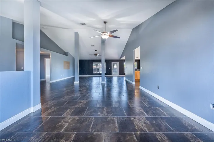 Unfurnished living room featuring high vaulted ceiling, dark tile flooring, and ceiling fan